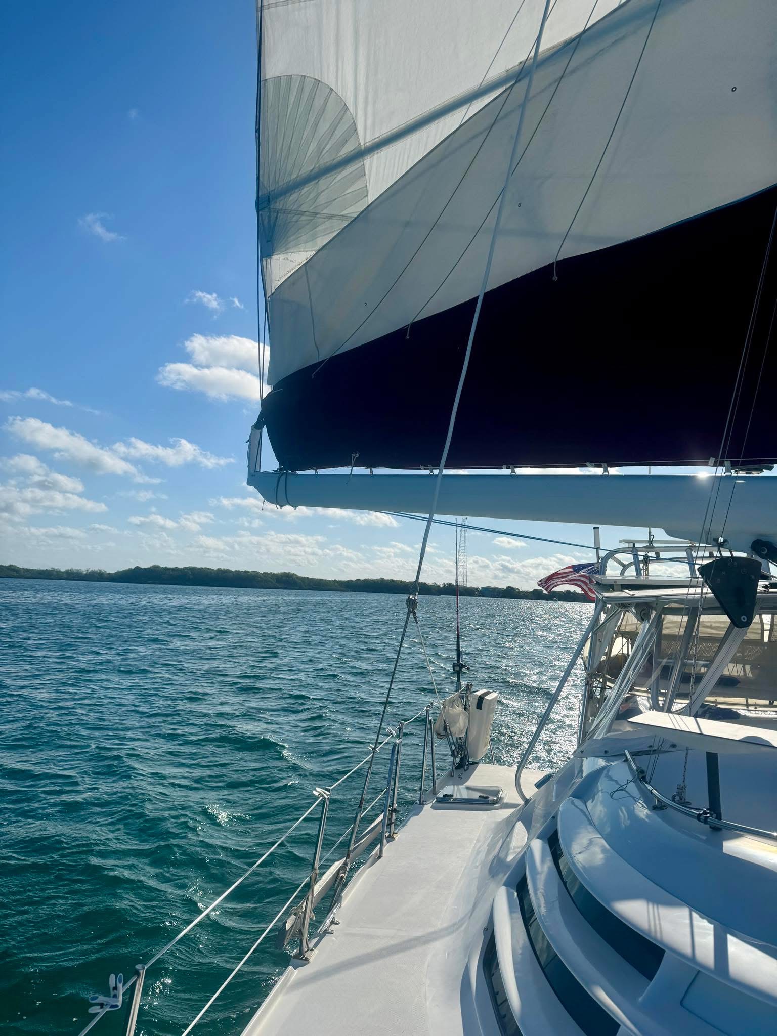 On deck view of Now and Zen catamaran sailing on the St Johns River with sails up and American flag
