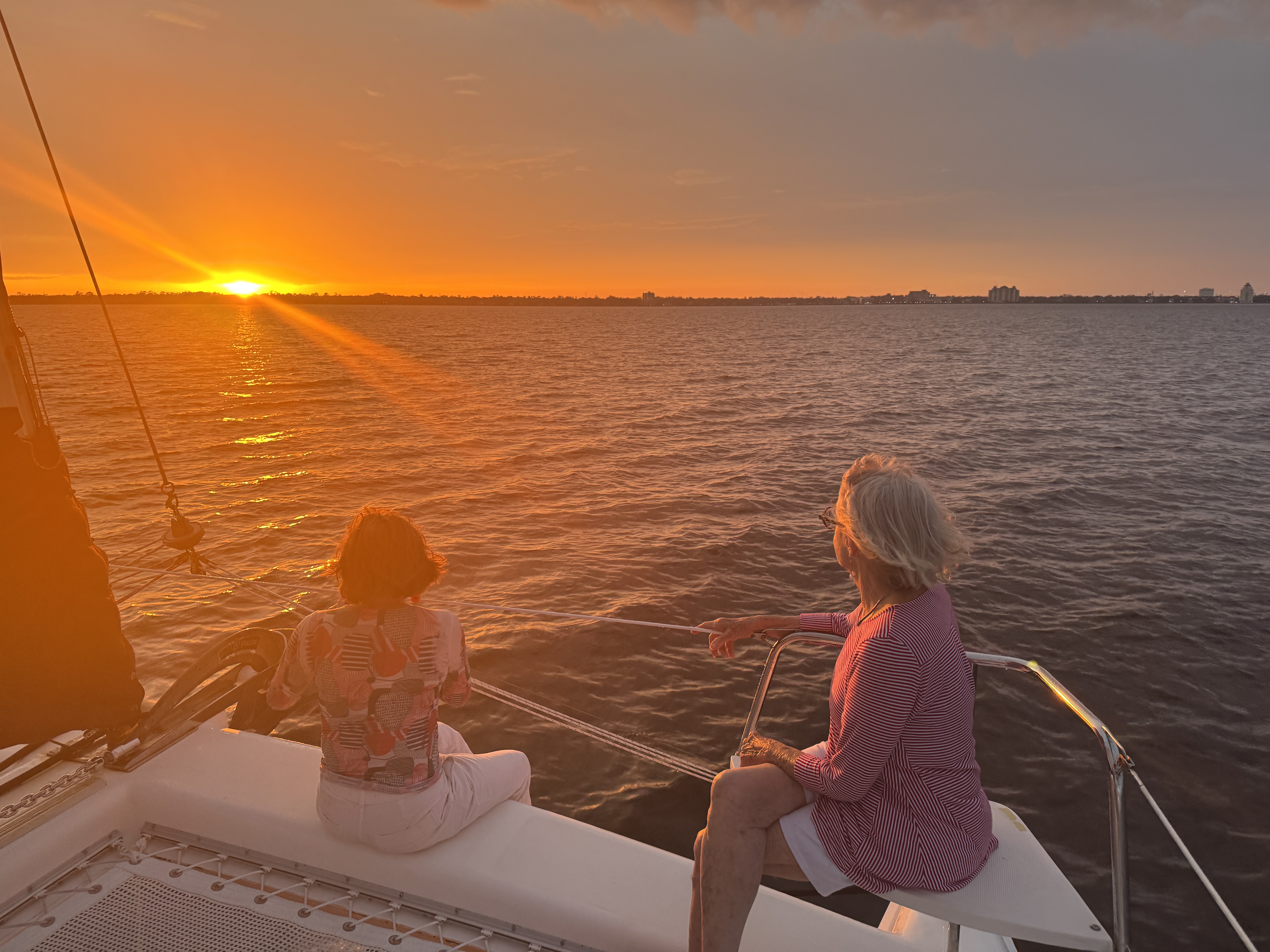 Two women watching a stunning orange sunset from the deck of Now and Zen catamaran on the St Johns River Jacksonville